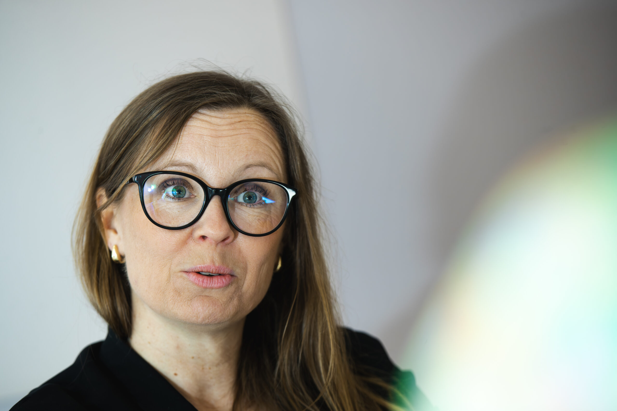 Lena Pireva med glasögon ser åt sidan mot neutral bakgrund.